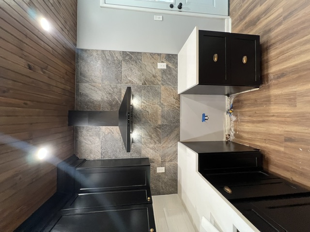 Kitchen remodel by Pittman Construction — black cabinets, stone tile backsplash, wall-mount range hood, wood plank ceiling